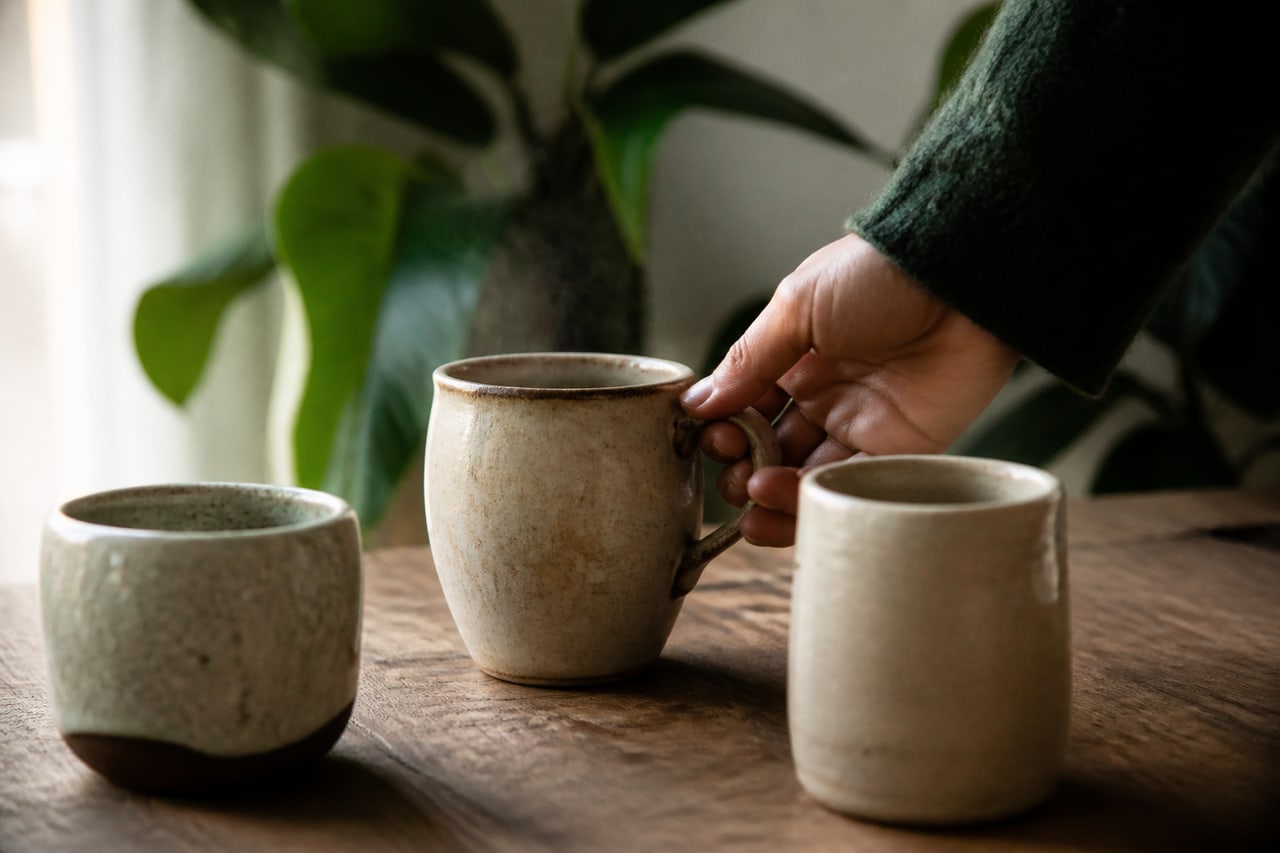 Una mano elige una taza de cerámica familiar entre otras dos sobre una mesa de desayuno.